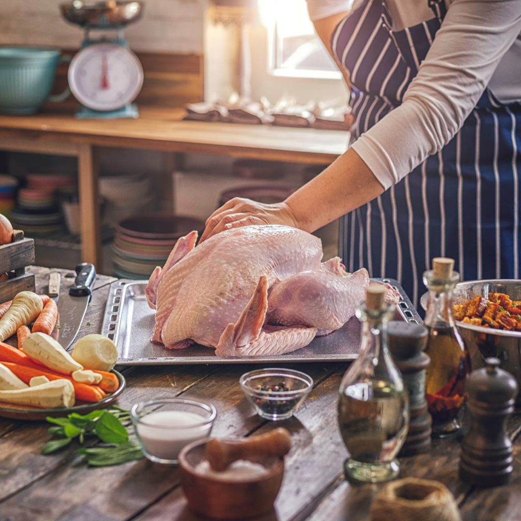 Person in apron prepping turkey on baking sheet, surrounded by vegetables and ingredients