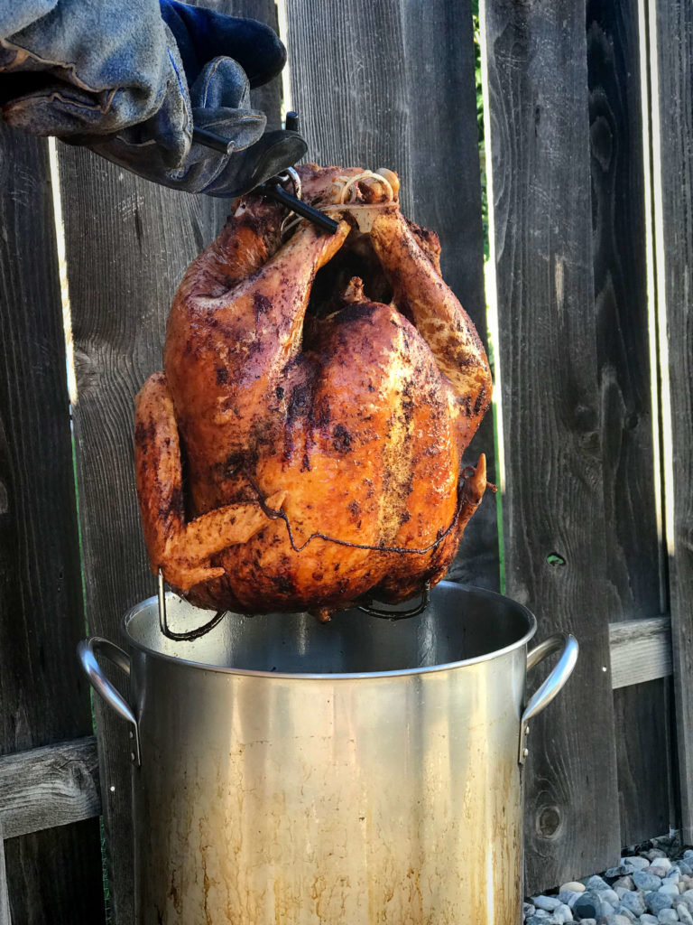 Deep-fried turkey being lowered into a pot of hot oil outdoors for a crispy golden finish