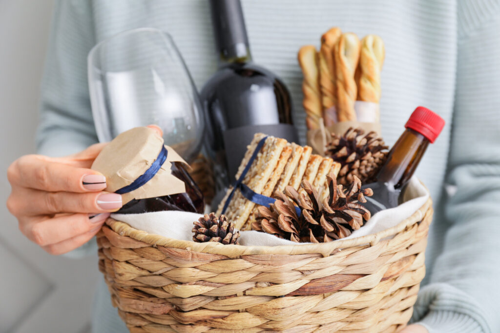 A woman holding an affordable holiday gift basket filled with wine, crackers, bread, jams and pine cones