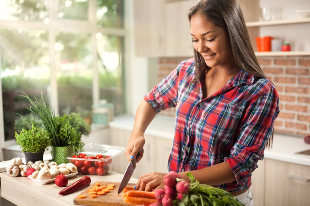 A woman with long hair cutting carrots and other root vegetables on a cutting board