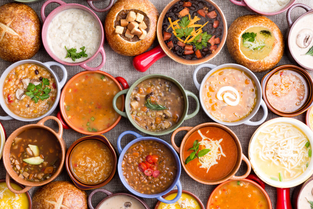 A variety of soups in handled containers and bread bowls, topped with various garnishes