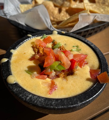 bowl of queso with tomatoes and pepper sitting next to a basket of tortilla chips