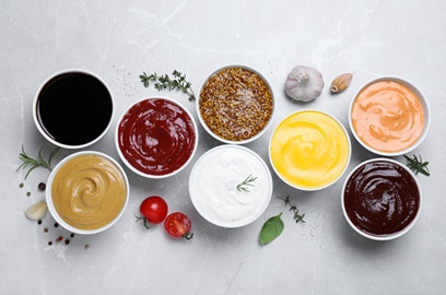 Eight sauces surrounded by fresh ingredients on a marble countertop