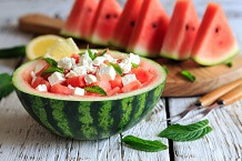 Hollowed-out watermelon holding a summer salad with sliced watermelon in the background
