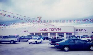 Cars parked in front of Food Town grocery store decorated with colorful flags