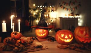Tabletop decorated with burlap, leaves, candles, spiders and lit jack-o-lanterns, with decorated living room in the back