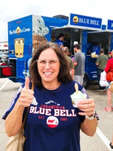 Woman in Blue Bell shirt holding Blue Bell ice cream and giving a thumbs-up sign