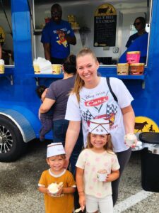 Woman with two children in paper ice cream hats holding cups of ice cream in front of a Blue Bell ice cream truck